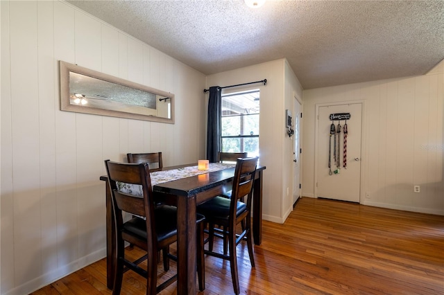 dining space with a textured ceiling, hardwood / wood-style flooring, and wooden walls