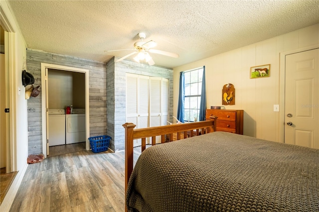 bedroom with ceiling fan, a textured ceiling, hardwood / wood-style flooring, washing machine and clothes dryer, and wood walls