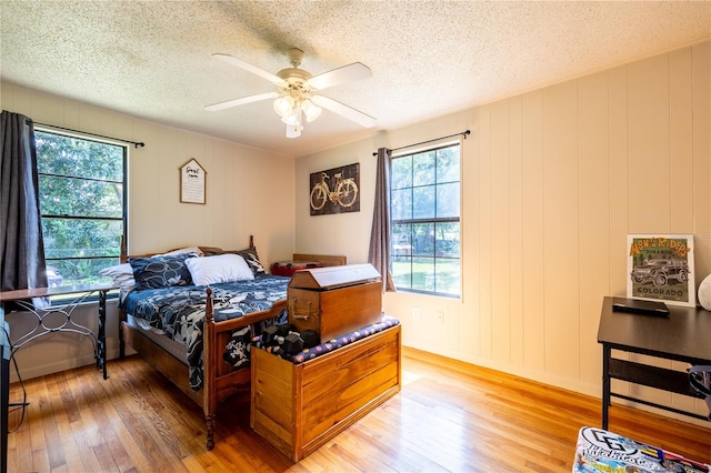 bedroom with a textured ceiling, hardwood / wood-style flooring, wooden walls, and ceiling fan