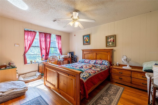 bedroom with ceiling fan, hardwood / wood-style flooring, a textured ceiling, and wooden walls