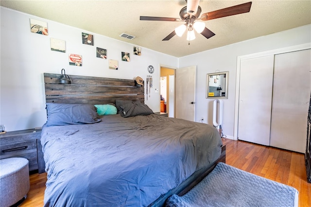 bedroom with a closet, a textured ceiling, wood-type flooring, and ceiling fan