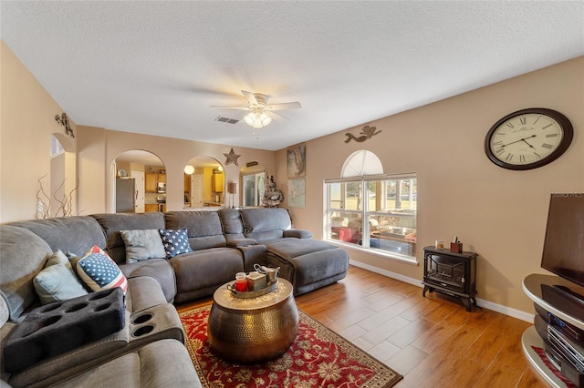 living room with ceiling fan, a textured ceiling, and light hardwood / wood-style flooring