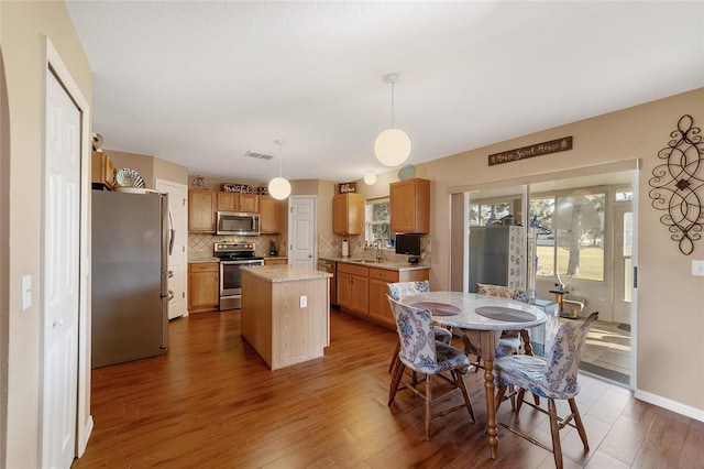 kitchen featuring appliances with stainless steel finishes, sink, a center island, pendant lighting, and dark hardwood / wood-style floors