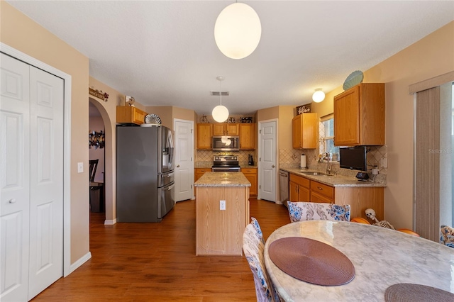 kitchen featuring hanging light fixtures, appliances with stainless steel finishes, dark wood-type flooring, sink, and a center island