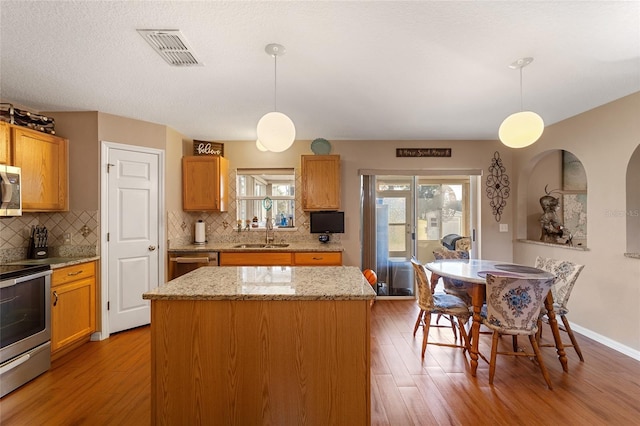 kitchen featuring a kitchen island, hardwood / wood-style flooring, decorative light fixtures, and stainless steel appliances