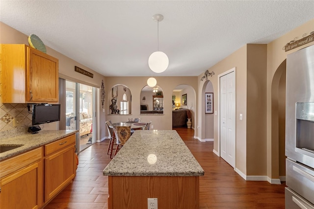 kitchen featuring tasteful backsplash, light stone countertops, a kitchen island, decorative light fixtures, and dark hardwood / wood-style floors