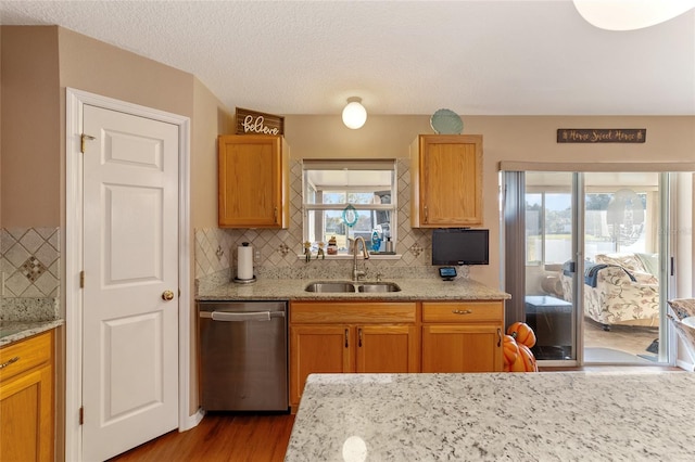 kitchen featuring light stone countertops, sink, wood-type flooring, dishwasher, and decorative backsplash