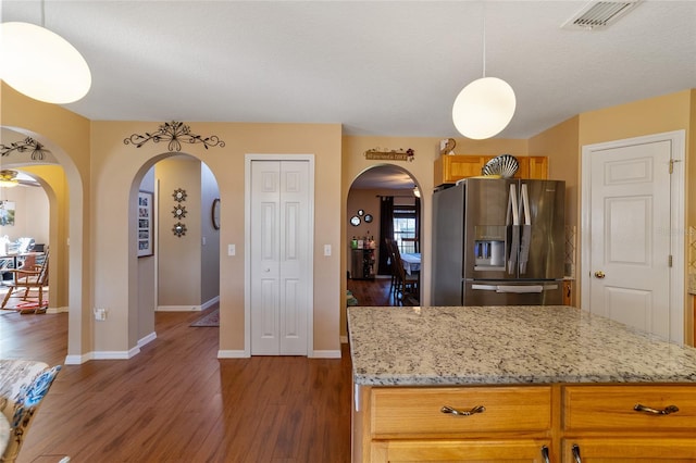 kitchen with light stone countertops, a textured ceiling, dark hardwood / wood-style flooring, stainless steel fridge, and decorative light fixtures