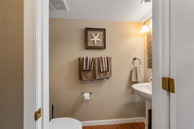 bathroom with a textured ceiling, wood-type flooring, and toilet