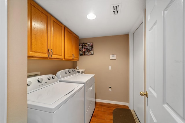 clothes washing area with washing machine and dryer, cabinets, and hardwood / wood-style floors