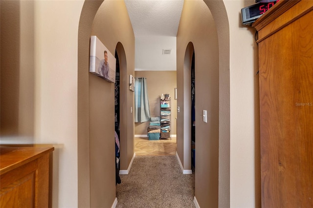 corridor with a textured ceiling and light colored carpet