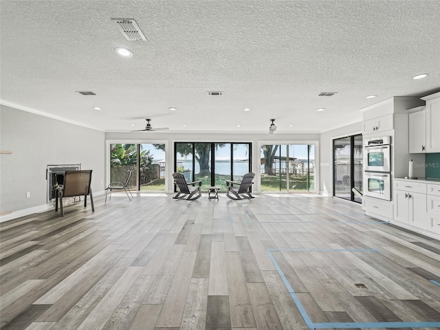 unfurnished living room with ornamental molding, light hardwood / wood-style flooring, a textured ceiling, and ceiling fan