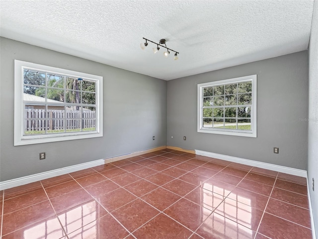 unfurnished room with dark tile patterned floors, a textured ceiling, and plenty of natural light