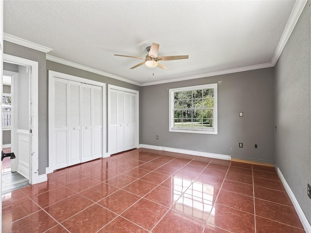 unfurnished bedroom featuring dark tile patterned flooring, ceiling fan, crown molding, and two closets