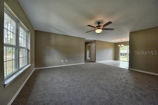 empty room with dark colored carpet and ceiling fan with notable chandelier