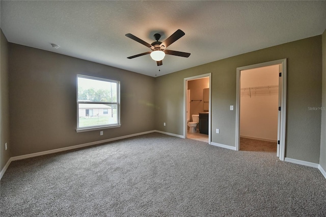 unfurnished bedroom with a closet, a spacious closet, light colored carpet, a textured ceiling, and ceiling fan