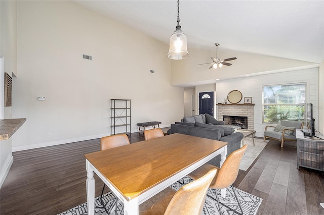 dining space featuring a brick fireplace, dark hardwood / wood-style floors, high vaulted ceiling, and ceiling fan