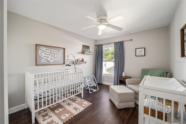 bedroom with dark hardwood / wood-style flooring, a nursery area, and ceiling fan