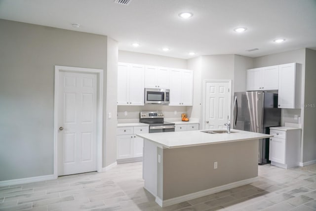 kitchen featuring light countertops, appliances with stainless steel finishes, white cabinetry, a sink, and an island with sink