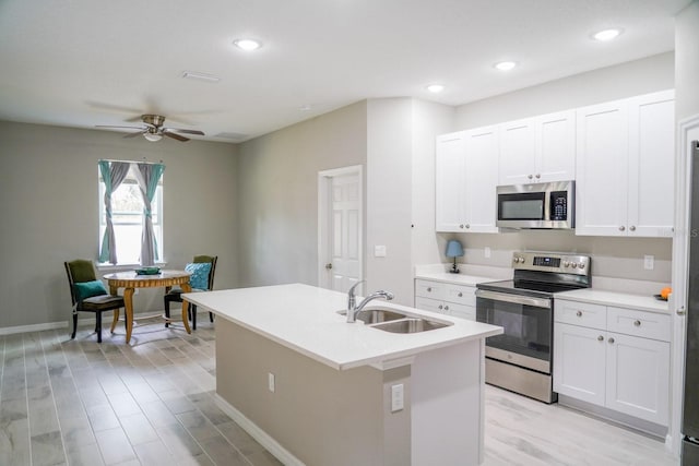 kitchen featuring stainless steel appliances, a sink, white cabinetry, light countertops, and a center island with sink