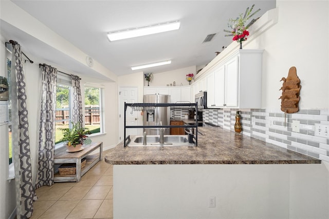 kitchen with lofted ceiling, kitchen peninsula, backsplash, appliances with stainless steel finishes, and white cabinetry