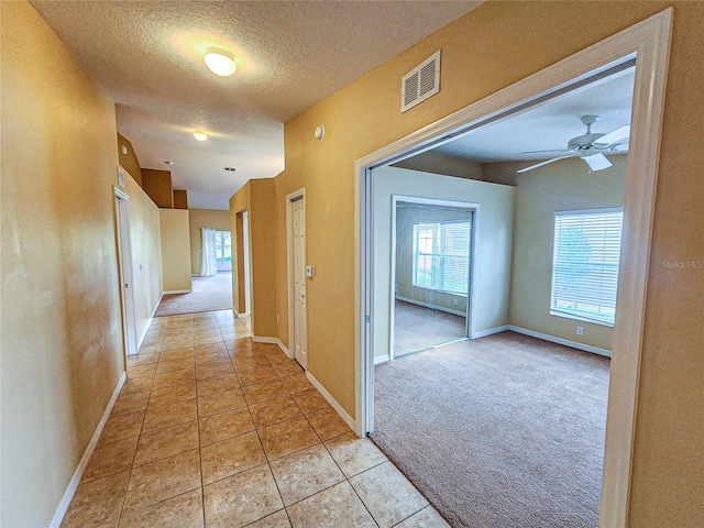 hall with light tile patterned floors, light colored carpet, visible vents, a textured ceiling, and baseboards