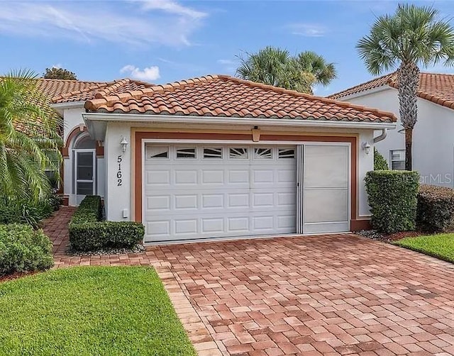 mediterranean / spanish-style house with a tiled roof, decorative driveway, an attached garage, and stucco siding