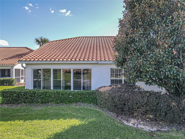 back of house featuring a yard, a tiled roof, and stucco siding