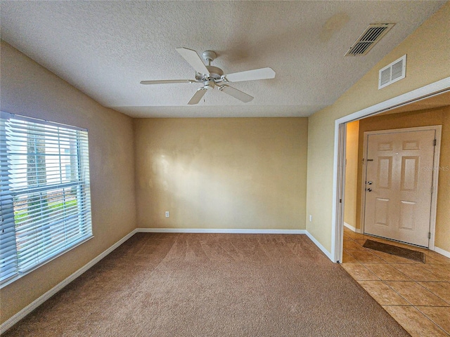 unfurnished room with light carpet, light tile patterned floors, visible vents, and a textured ceiling