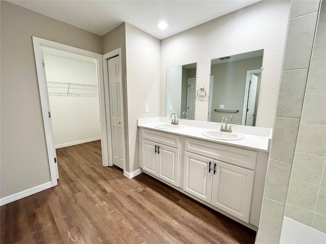 full bath featuring double vanity, wood finished floors, a sink, and a walk in closet