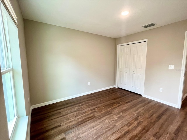 unfurnished bedroom with dark wood-style floors, baseboards, visible vents, and a closet