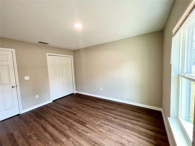 unfurnished bedroom with baseboards, a closet, visible vents, and dark wood-type flooring