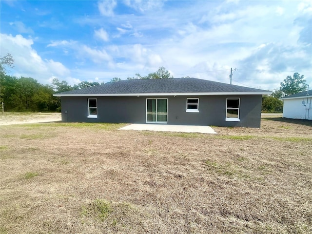 back of property featuring roof with shingles, a patio, a lawn, and stucco siding