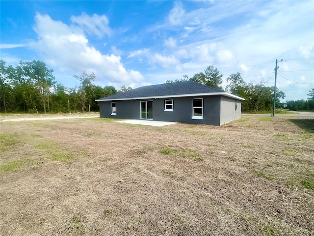 back of property with a shingled roof, a lawn, a patio area, and stucco siding