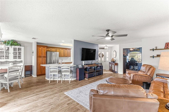 living room featuring sink, ceiling fan, a textured ceiling, and light hardwood / wood-style flooring