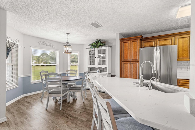 kitchen with tasteful backsplash, wood-type flooring, sink, decorative light fixtures, and stainless steel refrigerator