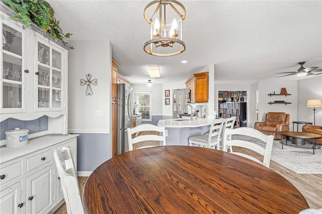 dining area with light hardwood / wood-style floors, a textured ceiling, sink, and ceiling fan with notable chandelier