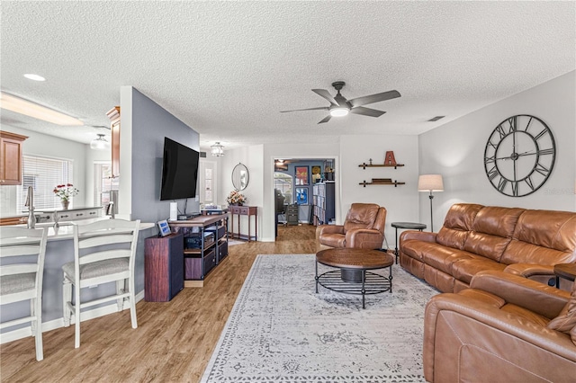 living room with a textured ceiling, light hardwood / wood-style floors, and ceiling fan