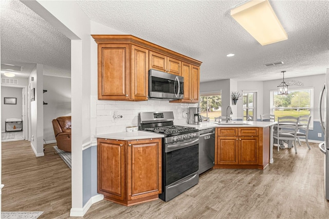 kitchen featuring light hardwood / wood-style floors, stainless steel appliances, a textured ceiling, and kitchen peninsula