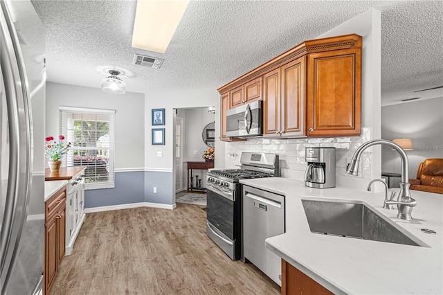 kitchen with appliances with stainless steel finishes, a textured ceiling, sink, and light wood-type flooring