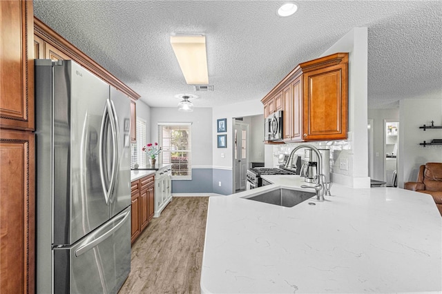 kitchen featuring sink, a textured ceiling, light hardwood / wood-style floors, stainless steel appliances, and decorative backsplash