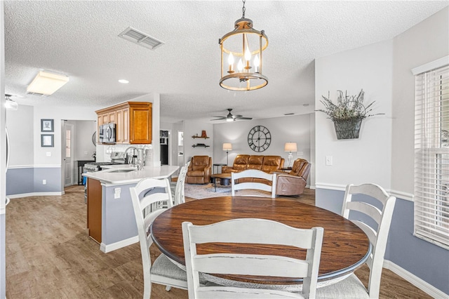 dining room with sink, a textured ceiling, light hardwood / wood-style flooring, and ceiling fan with notable chandelier