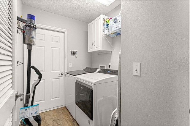 laundry area featuring cabinets, a textured ceiling, separate washer and dryer, and light wood-type flooring