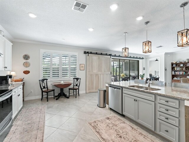 kitchen featuring sink, a barn door, stainless steel appliances, decorative light fixtures, and gray cabinets