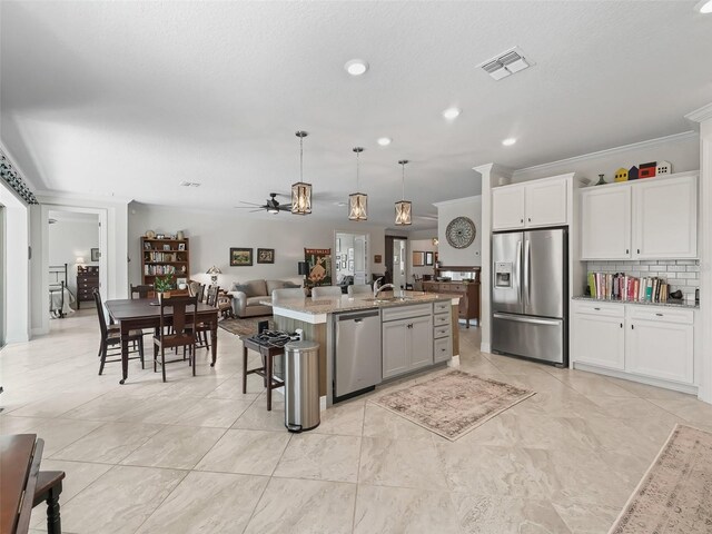 kitchen with a kitchen island with sink, stainless steel appliances, ornamental molding, decorative light fixtures, and white cabinetry