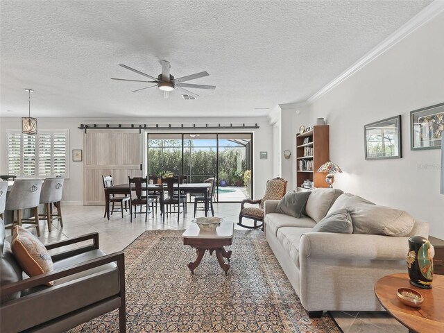 tiled living room featuring ceiling fan, a textured ceiling, ornamental molding, and a barn door