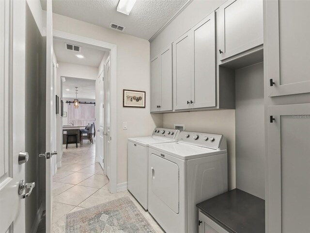 washroom with an inviting chandelier, light tile patterned floors, separate washer and dryer, a textured ceiling, and cabinets