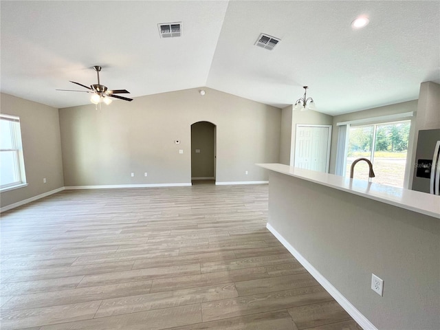 unfurnished room featuring arched walkways, vaulted ceiling, light wood-type flooring, and visible vents