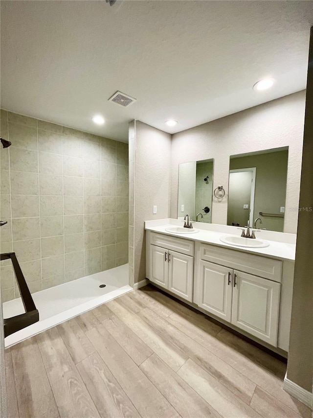 bathroom with double vanity, walk in shower, a sink, and wood finished floors