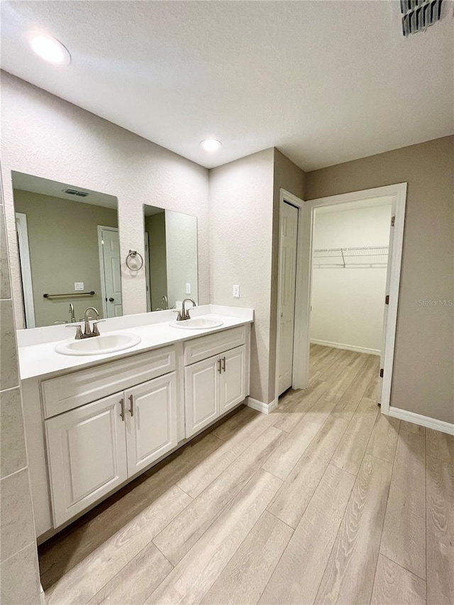 bathroom featuring double vanity, visible vents, a sink, and wood finished floors